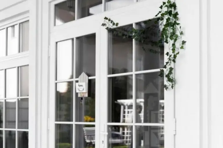 White glass-paneled entry door with matching sidelights, transom windows, and greenery draped above.